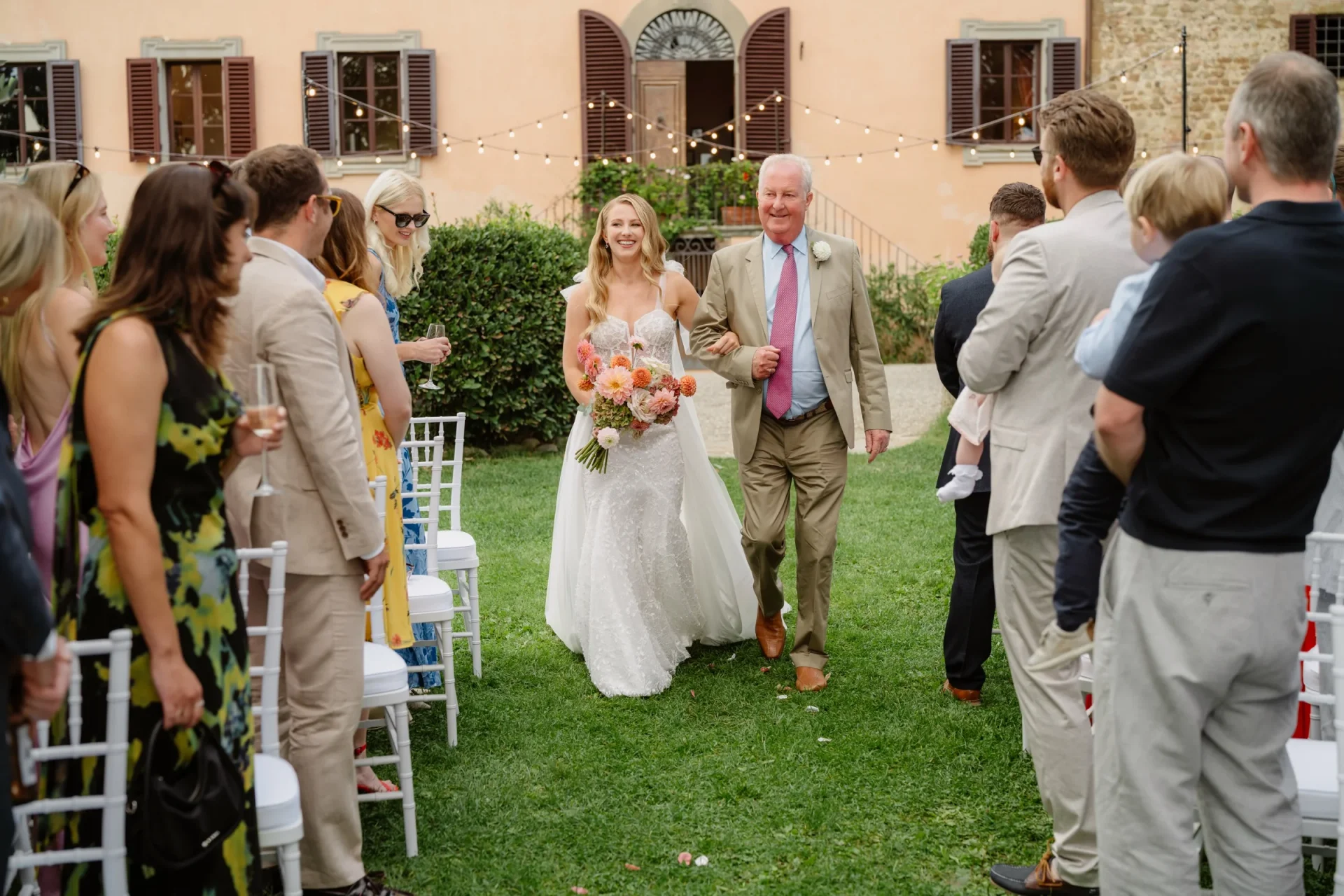 The bride walking up the aisle on her father's arm, guests turning to watch