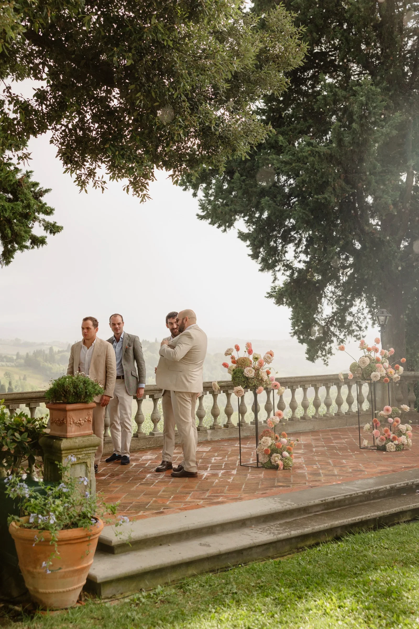 The groom and his groomsmen on the terrace, framed by the flowers and the old oak