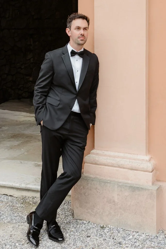 Groom in a black tuxedo leaning against a stone column