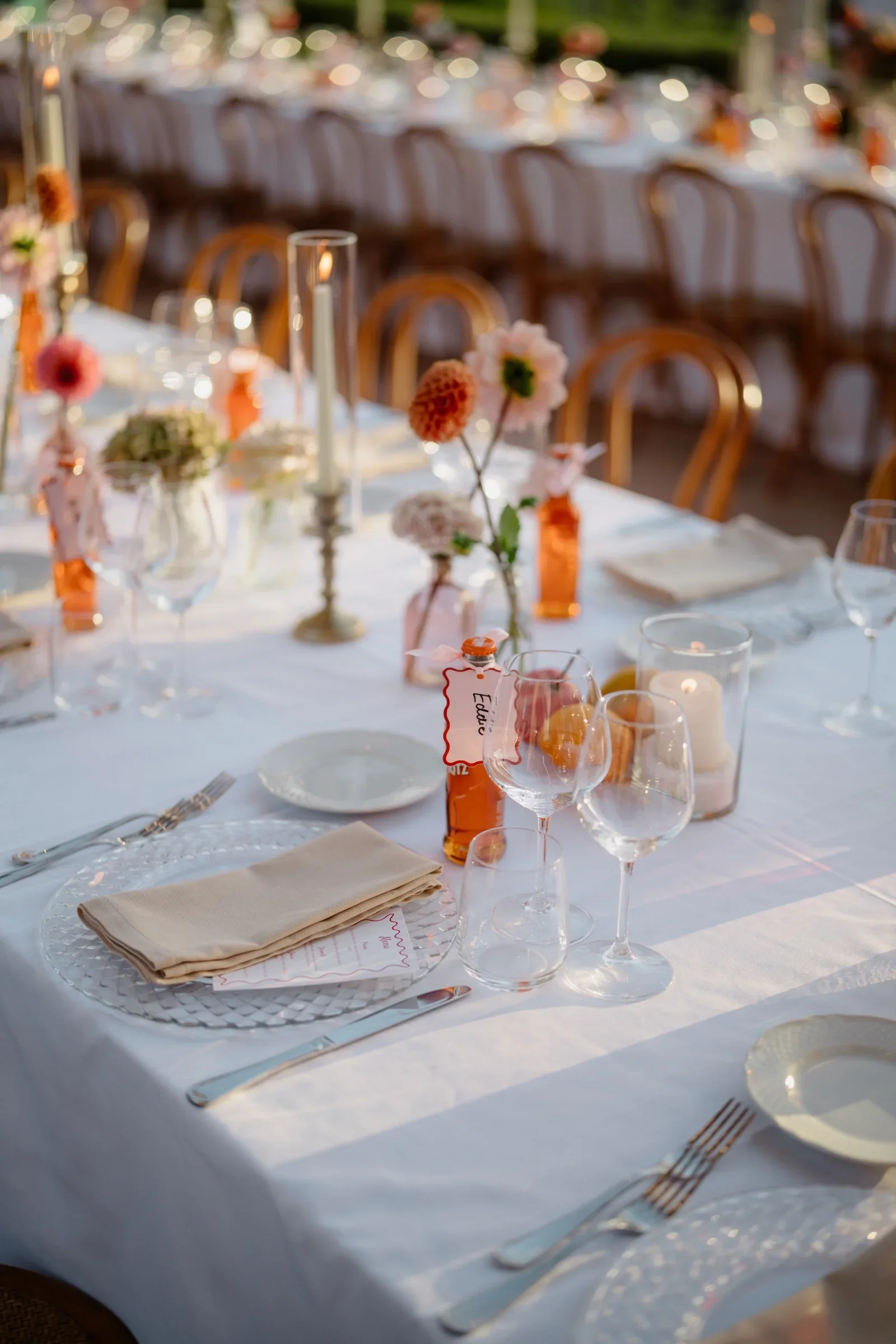 Dinner table set with coral and peach flowers, candles and blue linen
