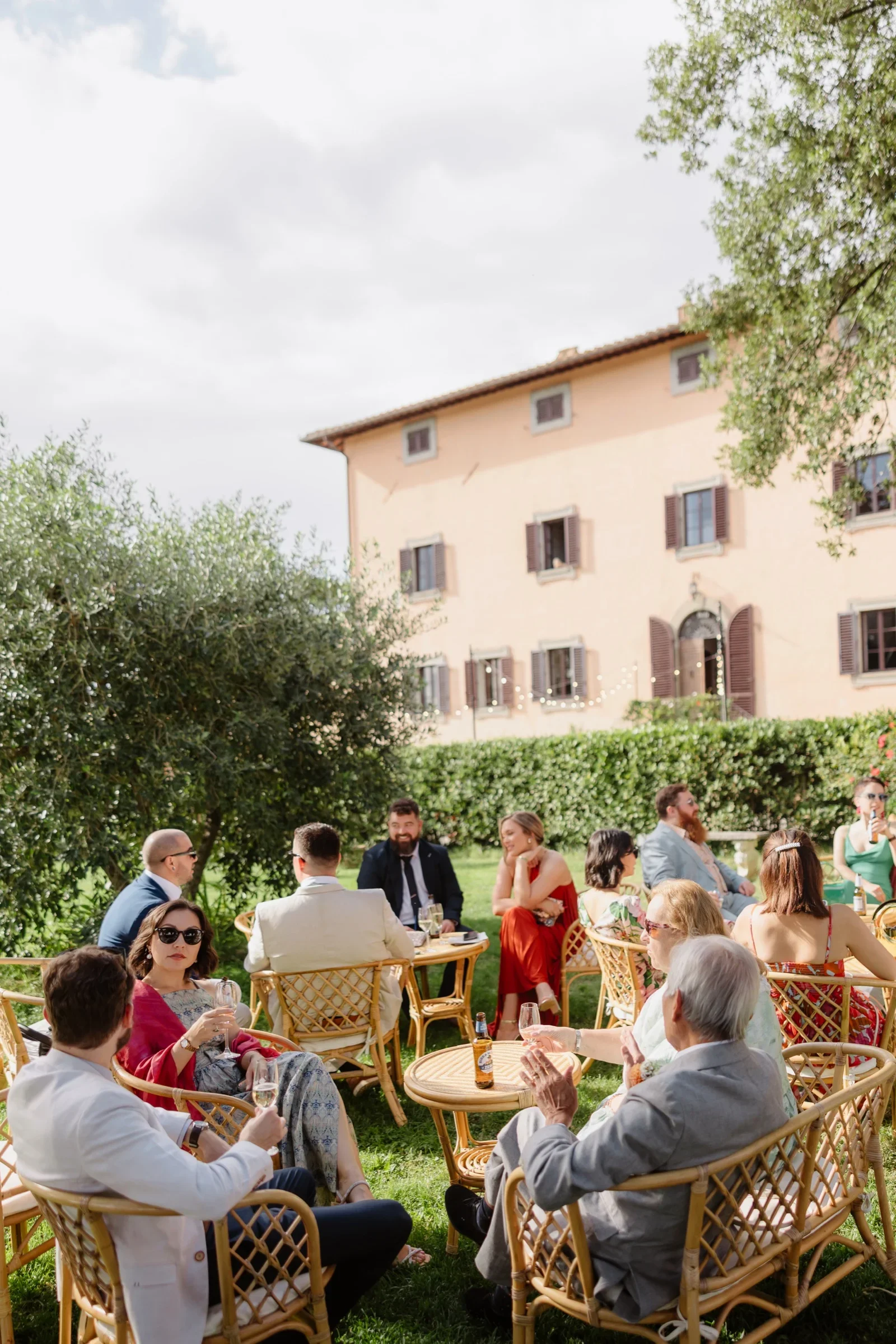 Guests seated in cane chairs on the lawn, the villa rising behind them
