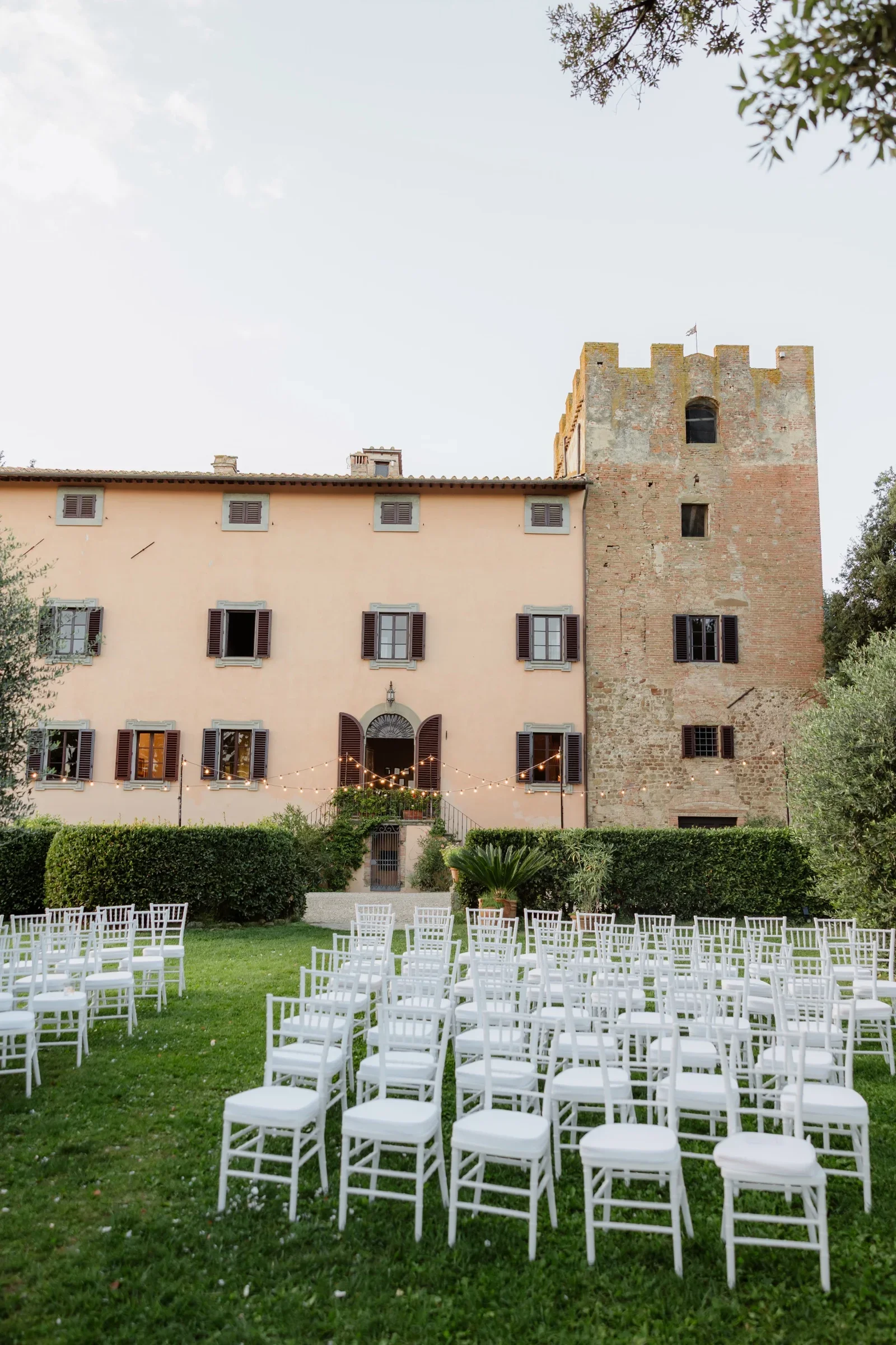Rows of white chairs set out on the lawn before the villa and tower